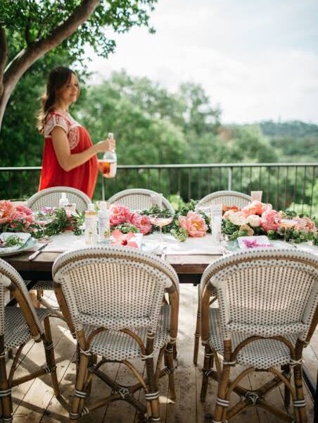 Loom Crafts Outdoor Garden Furniture A woman in a red dress is sitting at a table with flowers.